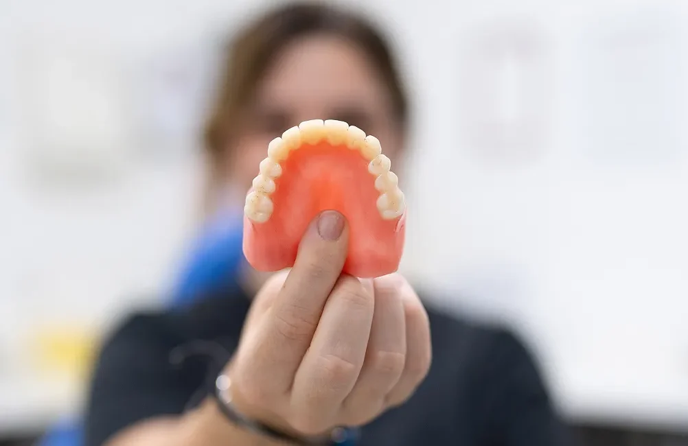 emergency-denture-repair Person holding a complete upper denture in front of the camera during a denture consultation.